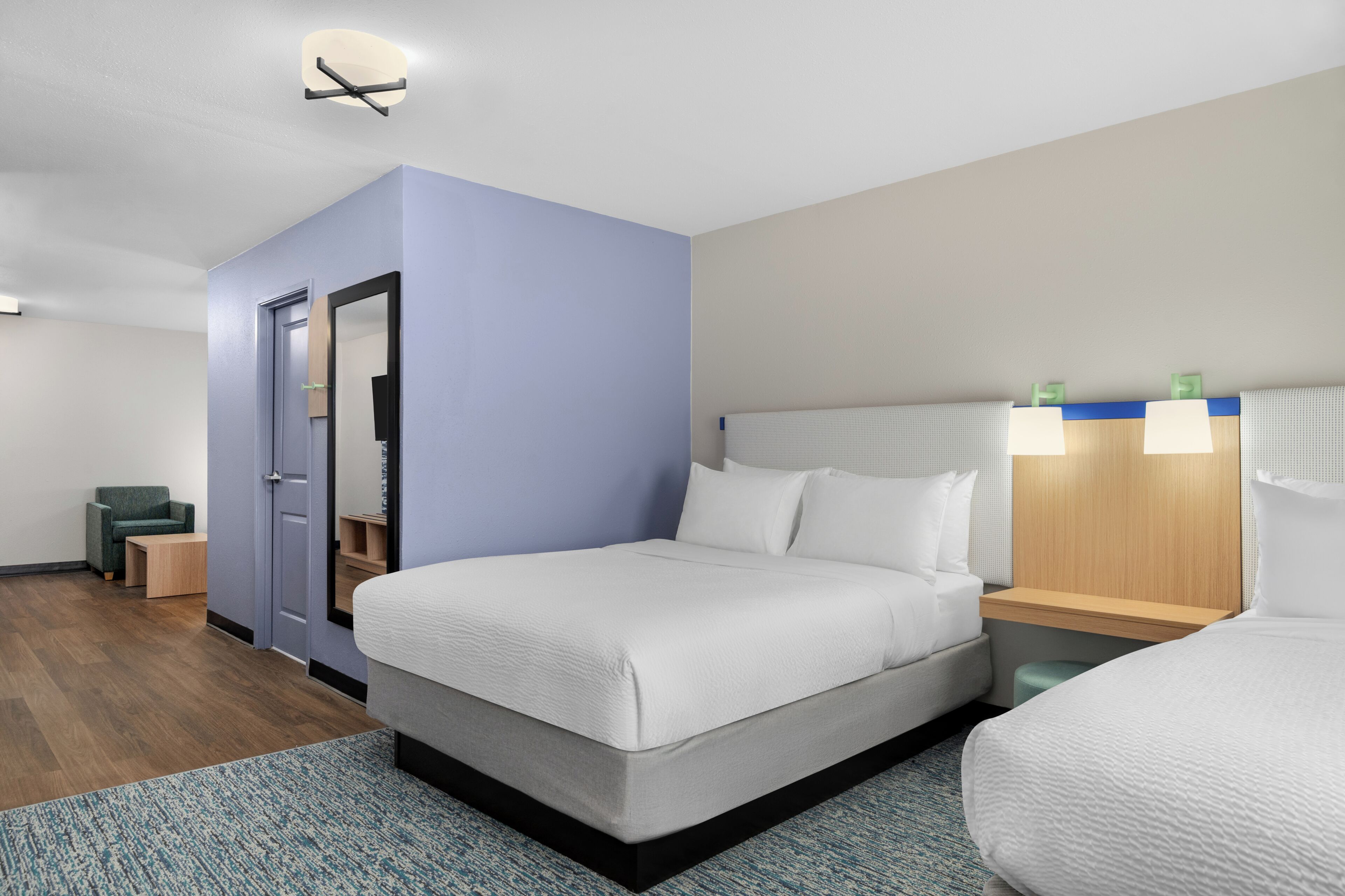Ett hotellrum med en stor säng, ett skrivbord, en stol, ett litet bord, en spegel och en dörr.