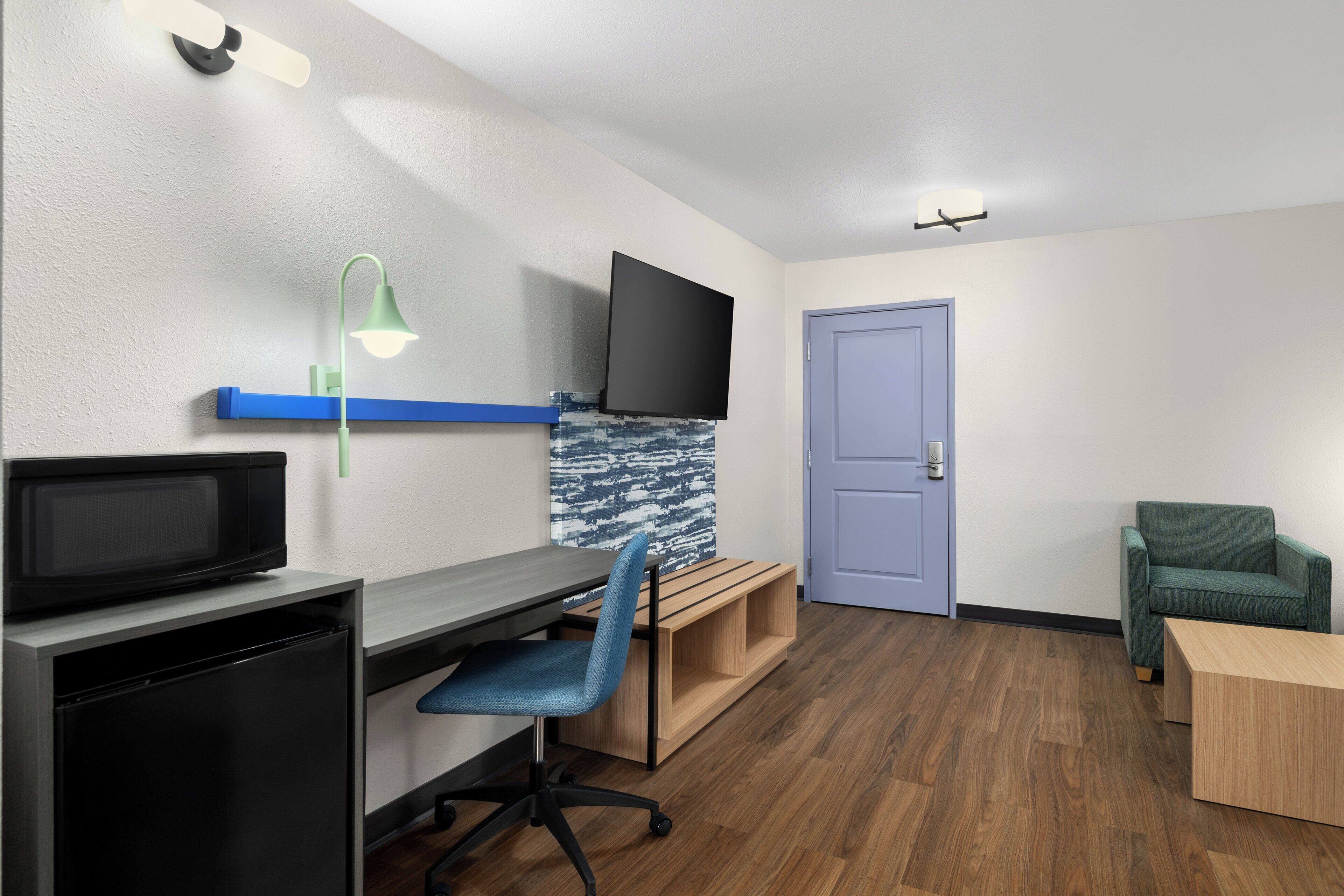 A room with a desk, chair, television, and a door.