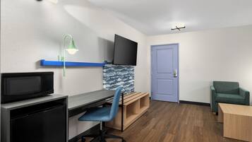 A room with a desk, chair, television, and a door.