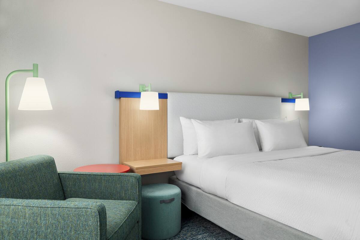 A hotel room with a bed, two bedside lamps, a nightstand, a green sofa, and a small round table.