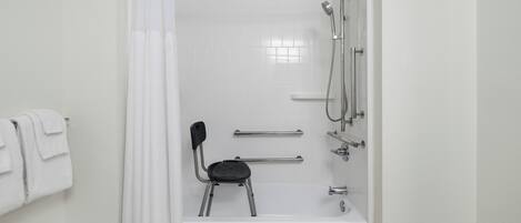 A bathroom with a shower, a chair, a towel rack, and a bathtub.