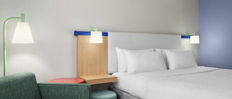 A modern hotel room with a bed, two bedside lamps, a nightstand, a green sofa, and a small round table.