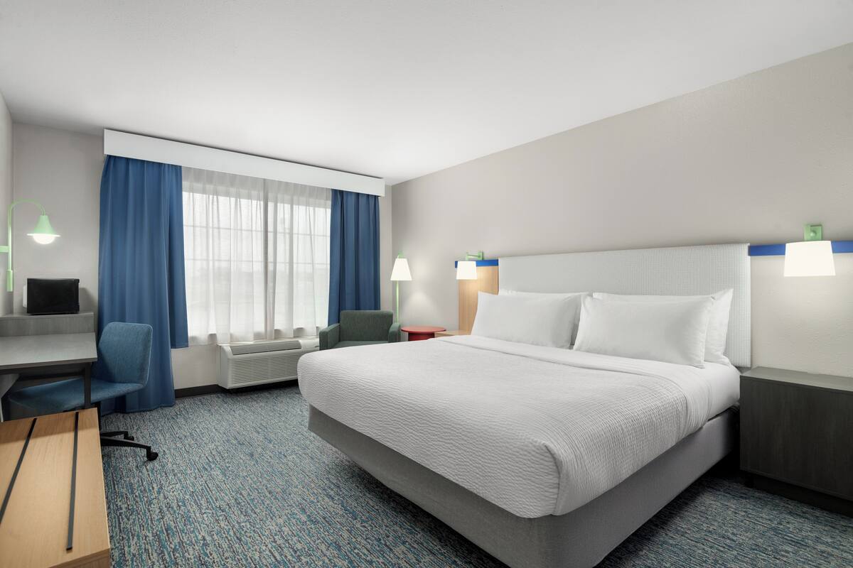 A hotel room with a bed, desk, chair, and two bedside lamps.