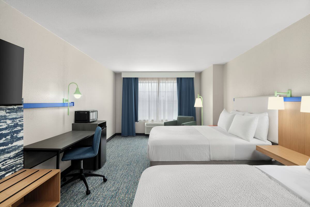 A hotel room with a desk, two beds, a TV, and a window with curtains.