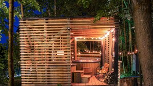 A wooden cabin with a hot tub and steps leading up to it, surrounded by trees.