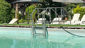 Piscina com plataforma de mergulho metálica, rodeada por espreguiçadeiras e guarda-sóis.