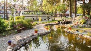 Um jardim tranquilo com um lago, rodeado por pedras e plantas em vasos.