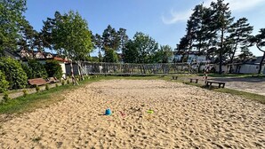 Uma área de praia arenosa com uma rede de voleibol, bancos e um parquinho.
