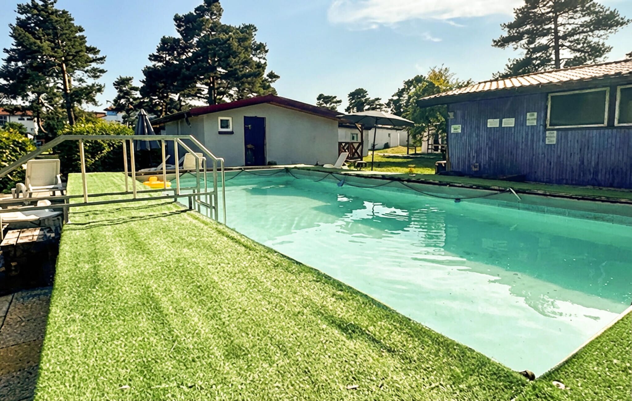 A swimming pool with a grassy area, lounge chairs, and a small building with a red roof.