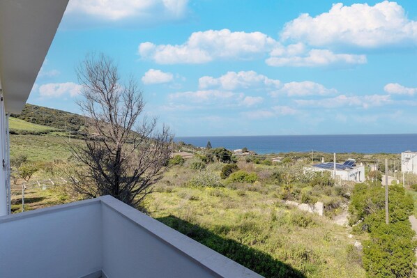 Un balcón con vista a un paisaje costero, que incluye un edificio con paneles solares y un cielo despejado.