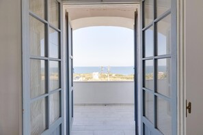 Puerta abierta que da a un balcón con vista al mar y edificios.