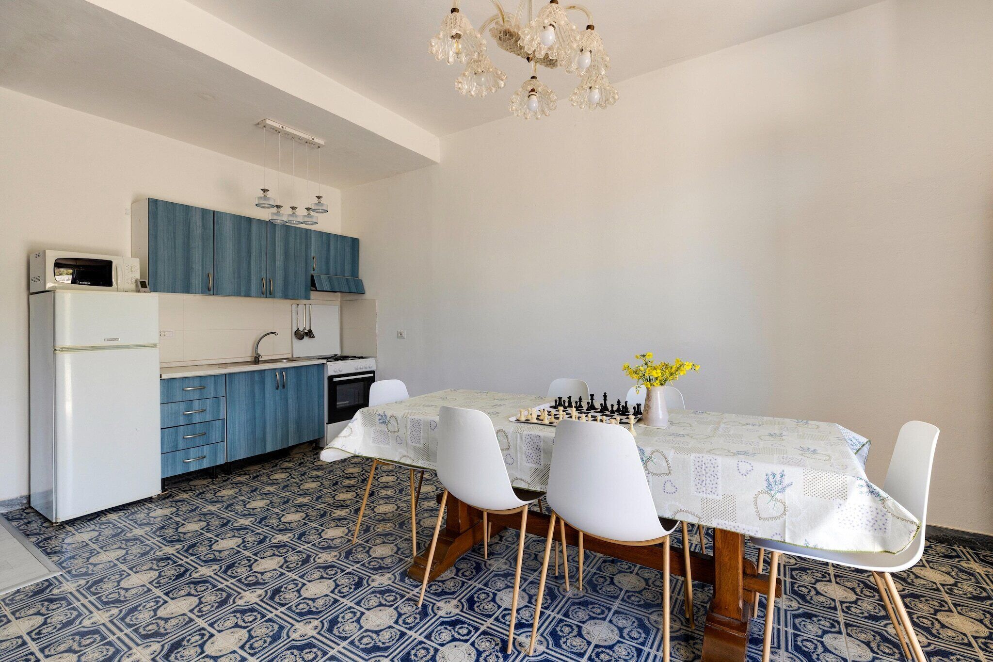 A compact kitchen with blue cabinets, a white refrigerator, and a dining table with white chairs.