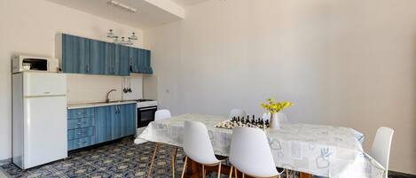 A compact kitchen with blue cabinets, a white refrigerator, and a dining table with white chairs.