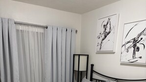 A neatly made bed with a patterned bedspread, a bedside table with a lamp, and two abstract wall art pieces.