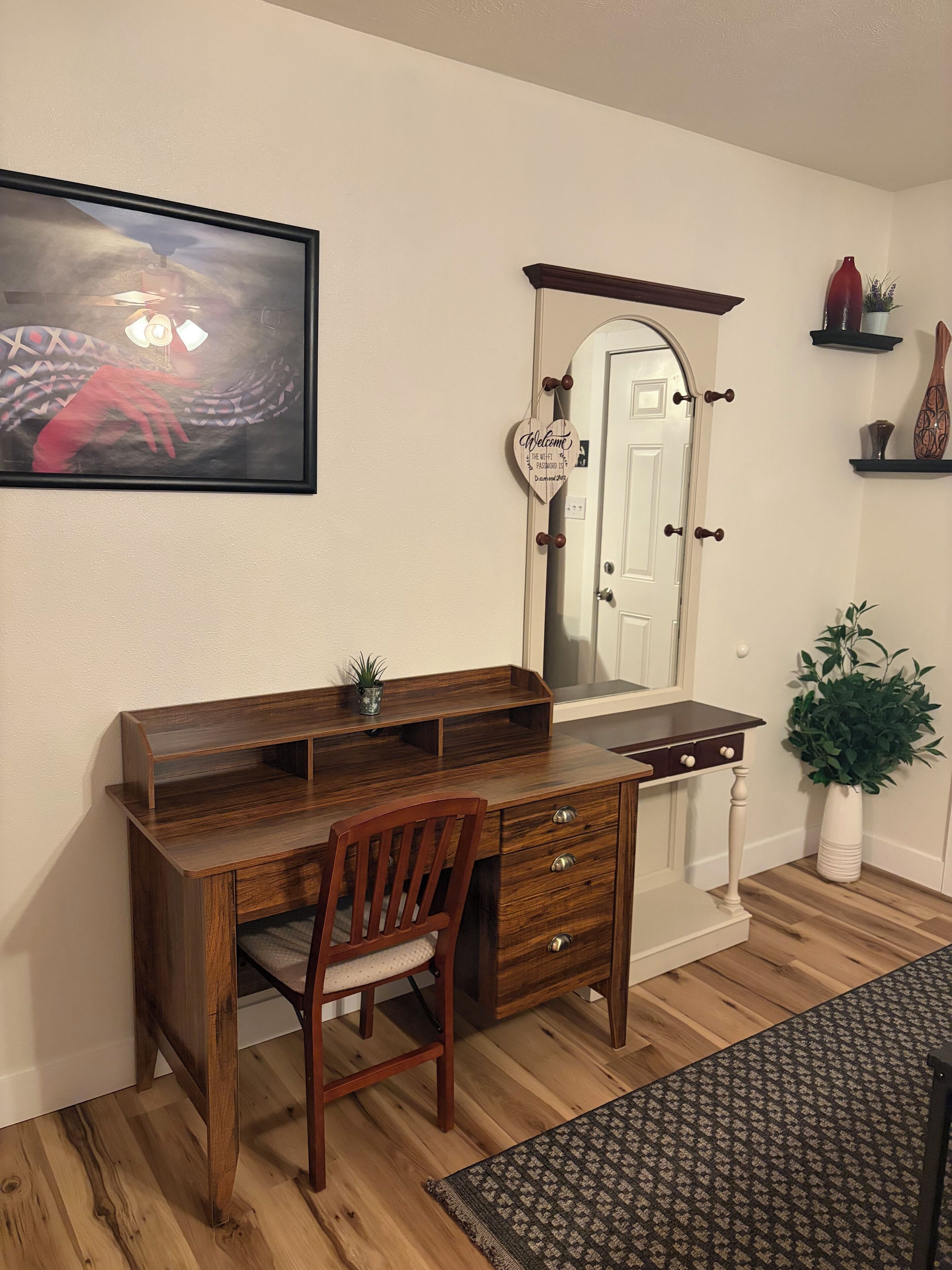 A wooden desk with drawers, a chair, a mirror, and a welcome sign.