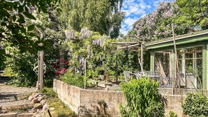 Ein Garten mit einer Pergola, einer Steinmauer und einem grünen Gebäude mit Fenstern.