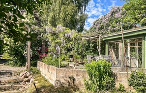 A garden with a pergola, a stone wall, and a green building with windows. - 5 bedroom beautiful home in Dalby (Dalby)