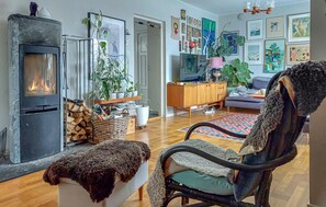 A cozy living room with a fireplace, a comfortable chair, a sofa, and a dining area with a wooden cabinet and a TV. - 5 bedroom beautiful home in Dalby (Dalby)