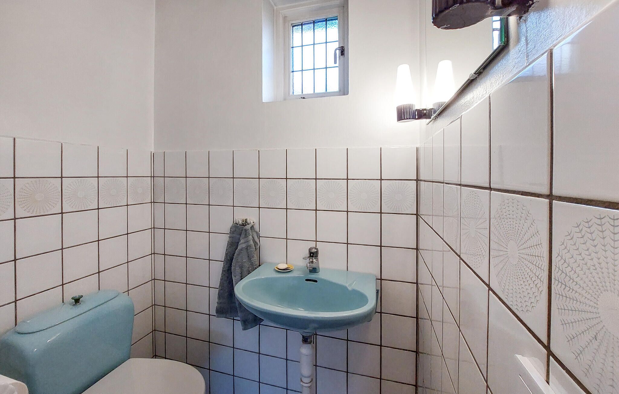 A bathroom with white tiled walls, a blue sink, a toilet, and a window with bars.