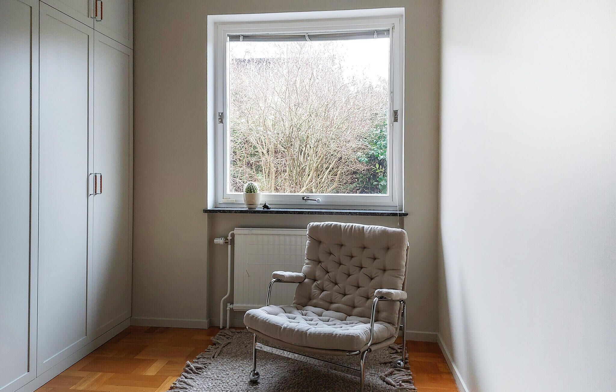 A corner room with a window, a radiator, a chair, and a cabinet.