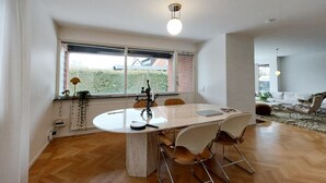 Un coin repas avec une table ronde, des chaises, une fenêtre donnant sur un espace verdoyant et un luminaire suspendu au plafond.