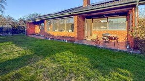 Une maison de plain-pied en briques, dotée de grandes fenêtres, d’un porche couvert et d’un petit jardin.