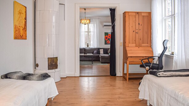 A room with two beds, a wooden cabinet, a chair, and a view into a living area with a sofa and a dining table. - Cozy home in Gärds Köpinge with WiFi (Gärds Köpinge)