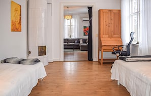 Et værelse med to senge, et træskab, en stol og udsigt til et opholdsområde med en sofa og et spisebord.