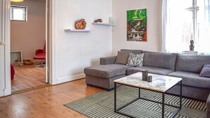 A living room with a grey sofa, a small coffee table, and a green striped rug. There are two shelves with decorative items and a painting on the wall. - Cozy home in Gärds Köpinge with WiFi (Gärds Köpinge)