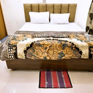 A bed with a floral bedspread, a headboard, and a striped rug. - Balaji Guest House (Varanasi)