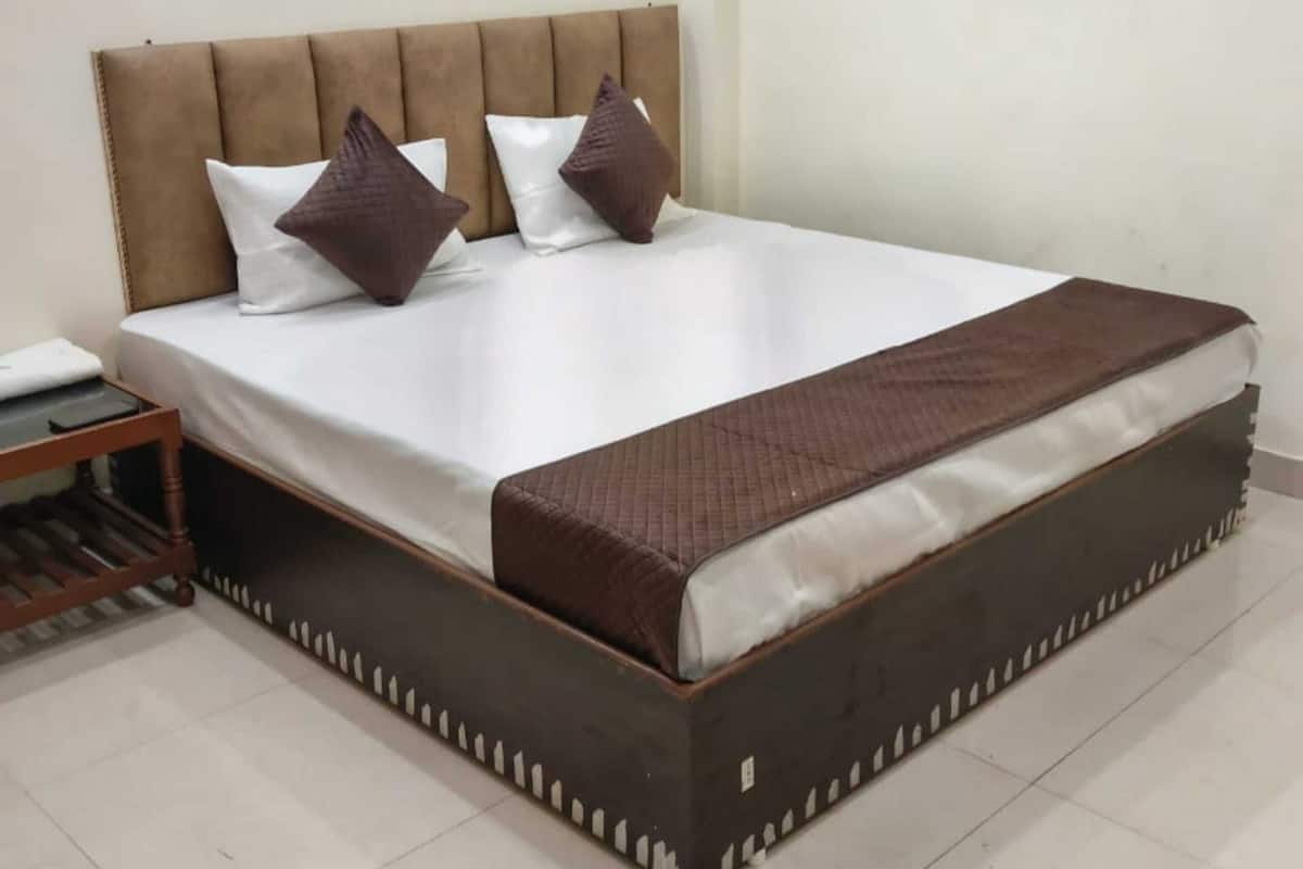 A neatly made bed with a padded headboard, a bedside table, and a bedside lamp.