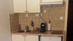 Eine kleine Küche mit weißen Schränken, einem Kühlschrank und einer Kaffeemaschine auf der Arbeitsplatte.