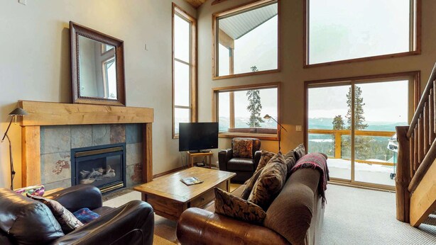 A spacious living room with a fireplace, leather furniture, a television, and large windows offering a scenic view. - Okanagan - Arolla Chalet D (Big White Mountain)