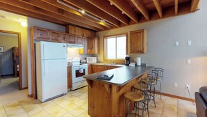 A kitchen with wooden cabinets, a refrigerator, a stove, a microwave, and a large island with bar stools. - Okanagan - Arolla Chalet D (Big White Mountain)