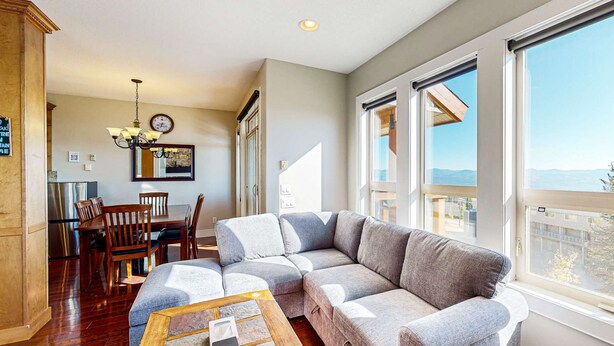 A spacious living area with a large sectional sofa, a dining table with chairs, and a kitchen area visible through an open door. - Okanagan - Aspens Townhouse 1 (Big White Mountain)