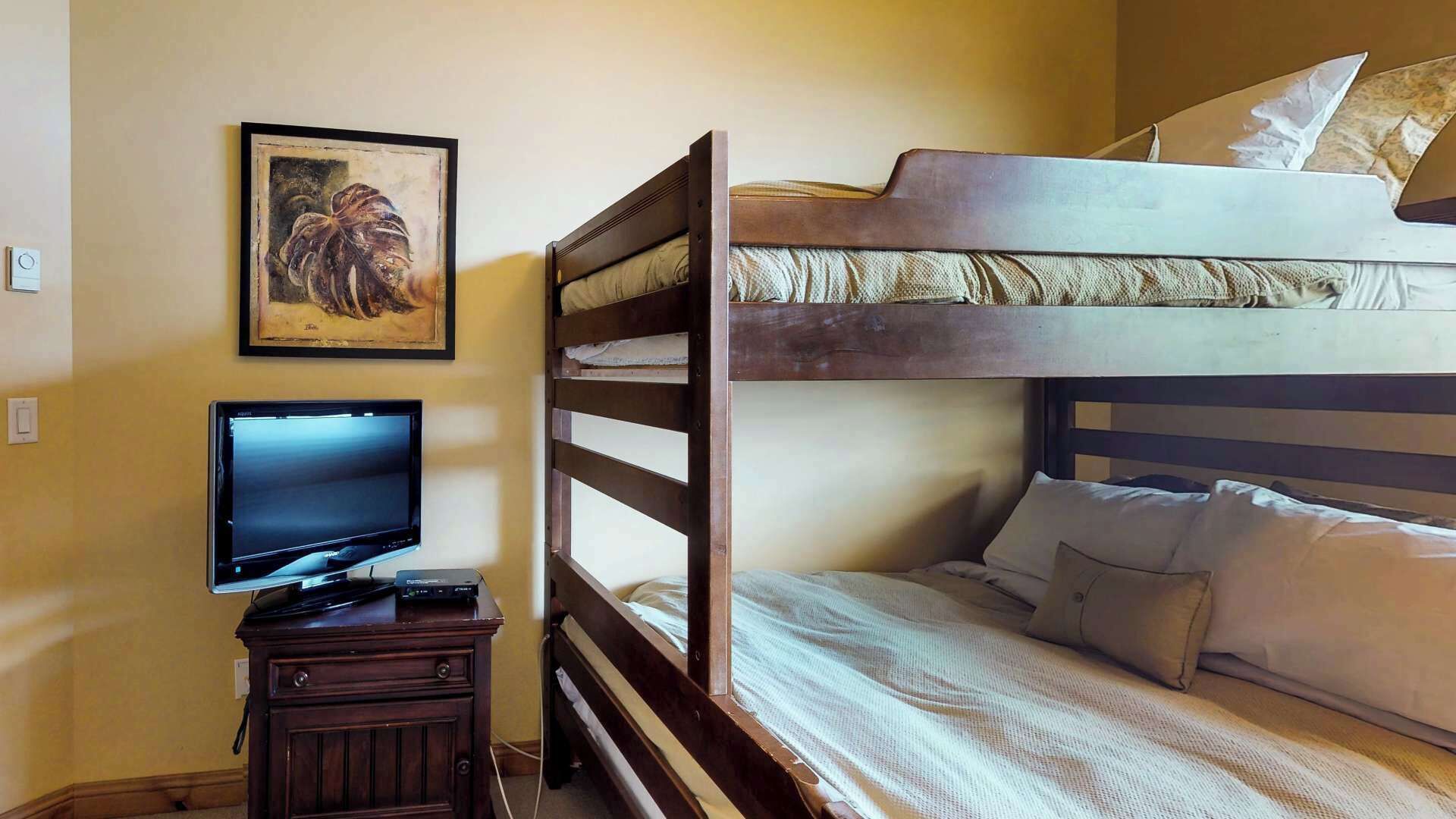 Een kamer met een stapelbed, een televisie op een houten standaard, en een schilderij in een lijst aan de muur.