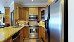 A kitchen with wooden cabinets, stainless steel appliances, granite countertops, and a built-in oven. - Okanagan - Aspens 4605 (Big White Mountain)