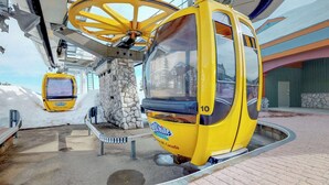 A yellow cable car at a station with a stone wall and a building in the background. - Okanagan - Aspens 4307 (Big White Mountain)