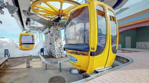 Um teleférico amarelo numa estação, com um muro de pedra e um edifício ao fundo.