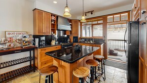 Een moderne keuken met houten kastjes, een groot eiland met krukken, een koffiehoek en uitzicht op buiten.