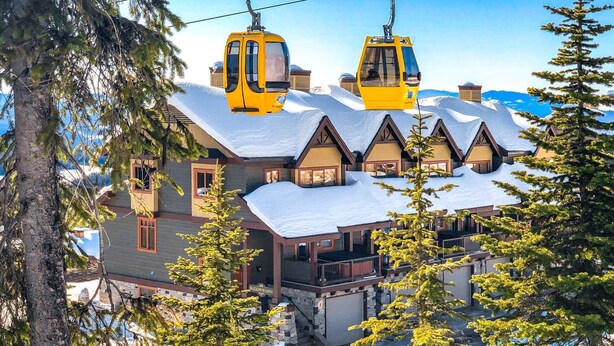 Een chalet met een met sneeuw bedekte dak, houten gevel en een kabelbaan.