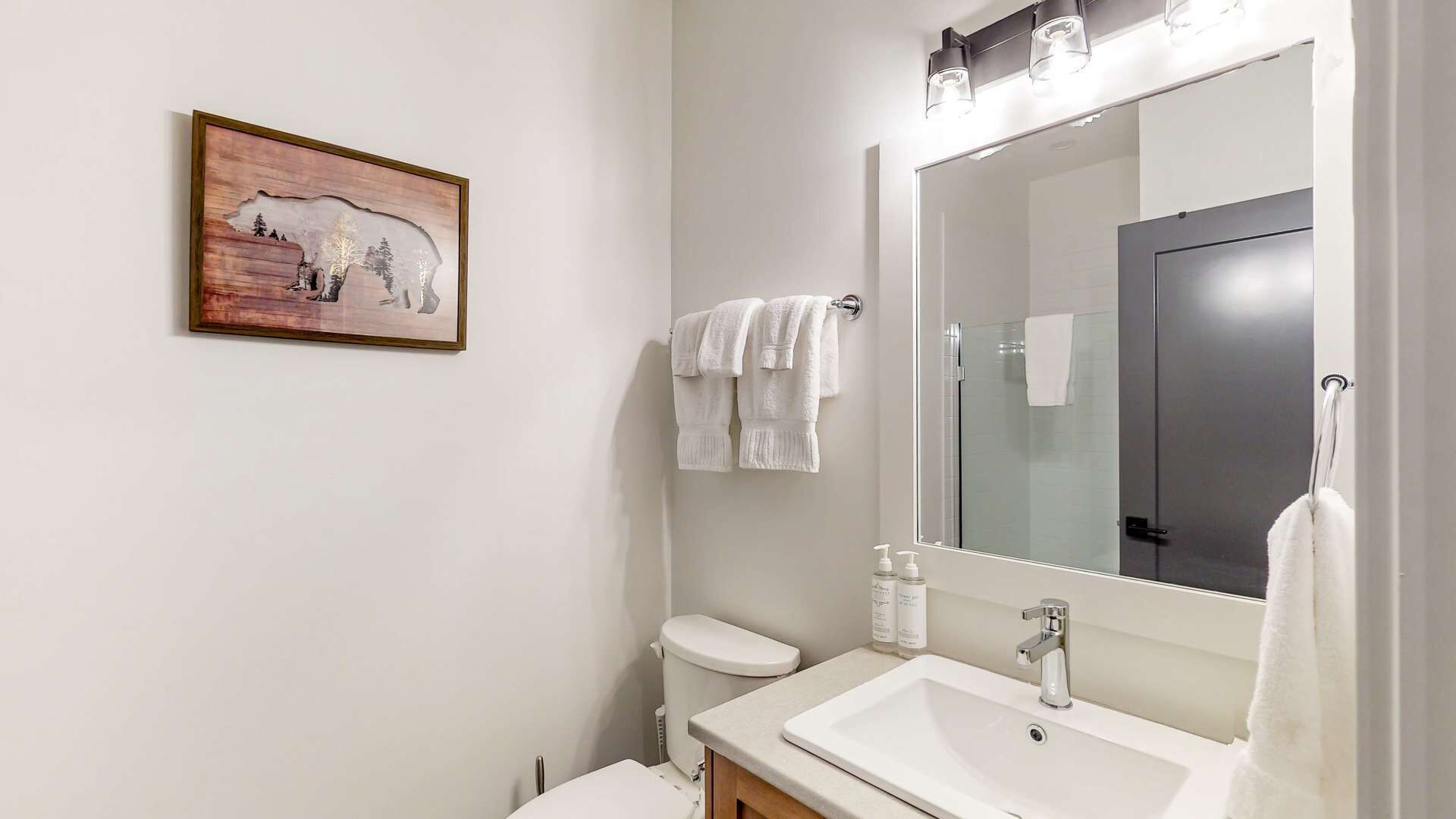 Un baño con un espejo grande, un lavamanos blanco y un inodoro. Hay un cuadro en la pared y toallas colgadas.