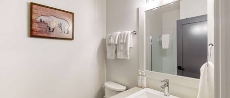 Un baño con un espejo grande, un lavamanos blanco y un inodoro. Hay un cuadro en la pared y toallas colgadas.