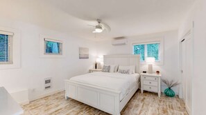 A bedroom with a white bed, bedside tables, a ceiling fan, and two windows with blinds. - Okanagan - Brooks Lake House (Christina Lake)