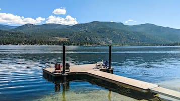 Une jetée en bois s’étendant dans un lac aux eaux cristallines, entourée de montagnes et d’arbres.