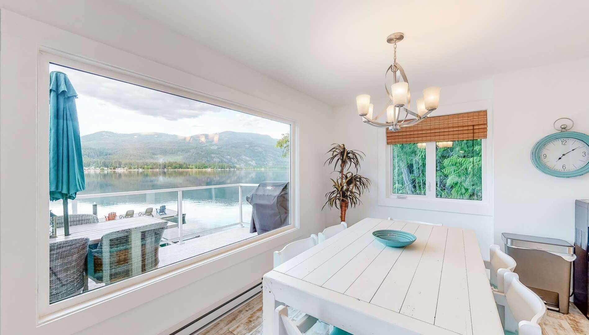 Un coin repas avec vue sur un lac, une table avec des chaises, un lustre et une horloge au mur.