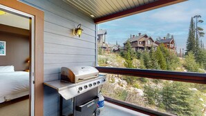 A room with a grill, a bed, and a view of houses and trees. - Okanagan - Glacier Lodge 103 (Beaverdell)