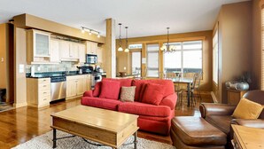 A modern kitchen with wooden cabinets, a red sofa, and a dining area with a table and chairs. - Okanagan - Glacier Lodge 106 (Beaverdell)