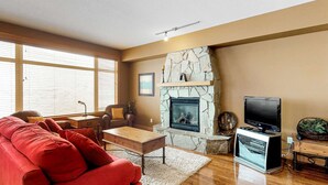 A living room with a fireplace, a television, and a red sofa. - Okanagan - Glacier Lodge 106 (Beaverdell)