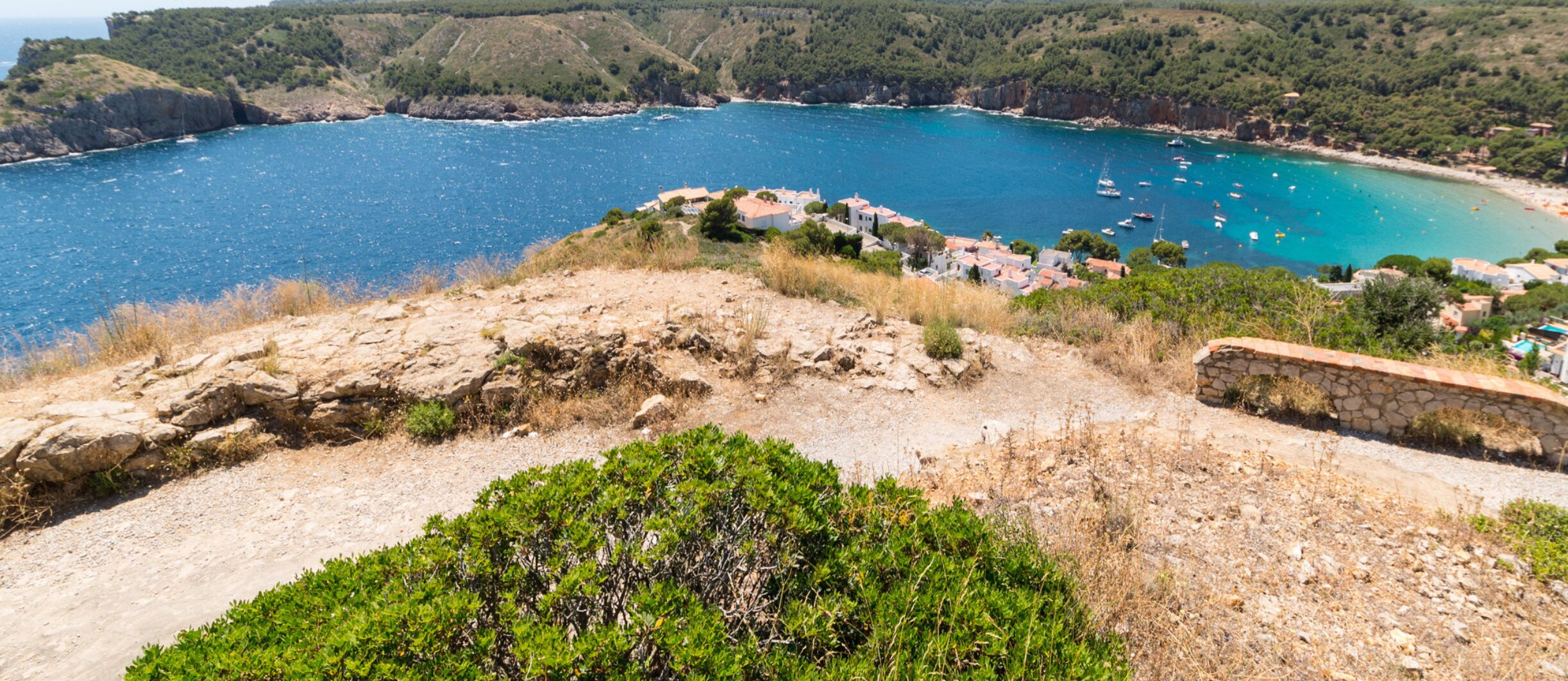 A coastal village with stone houses, a clear view of the sea, and a rocky path leading to the beach.